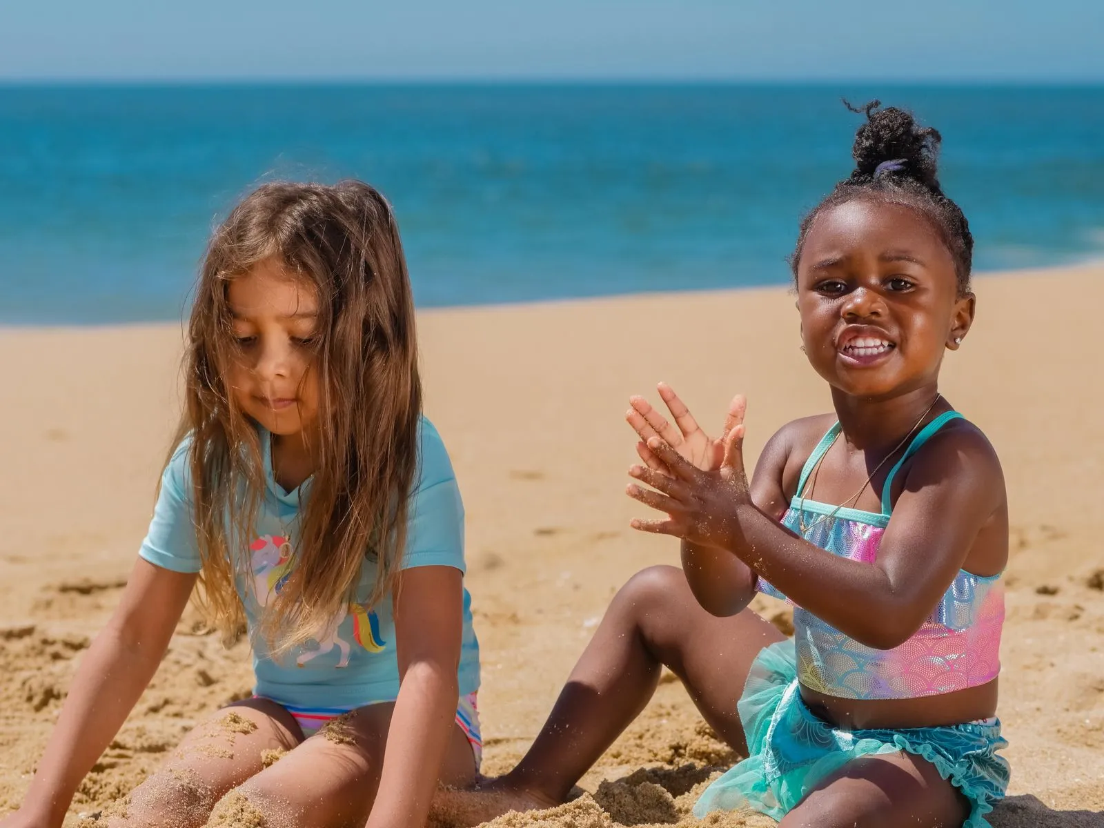 Two young girls playing in the sand on a sunny Southern California beach, ocean in the background